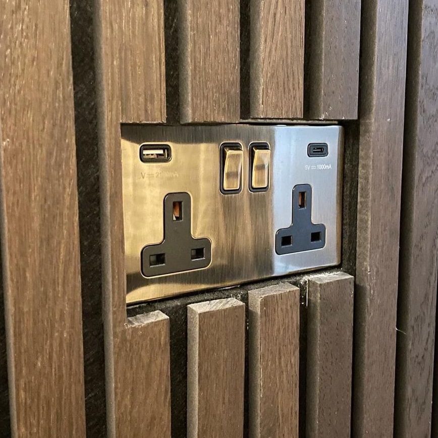 A plug socket sunken behind some acoustic wood panelling