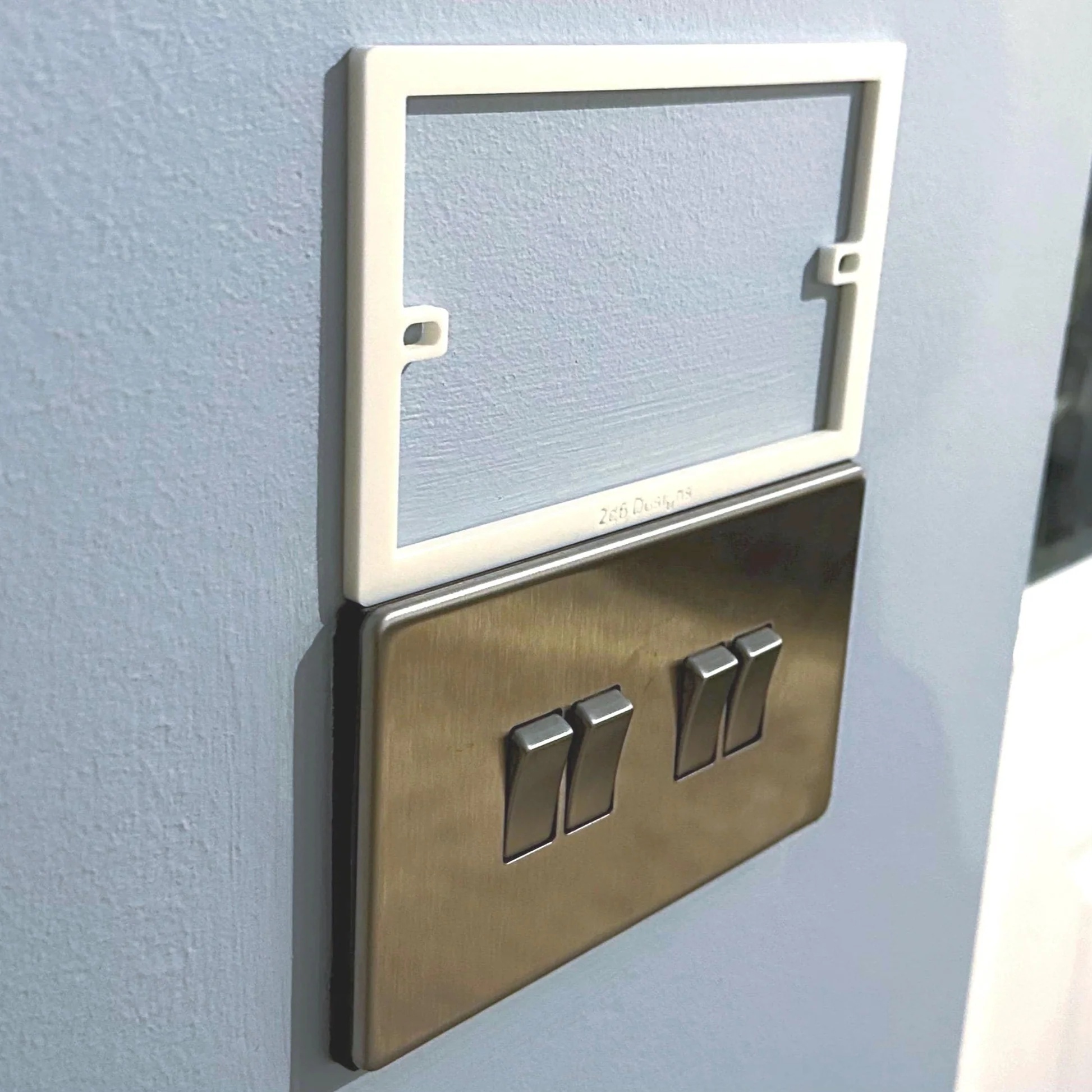 Socket spacer fitted behind a UK double gang light switch, with another alongside for reference